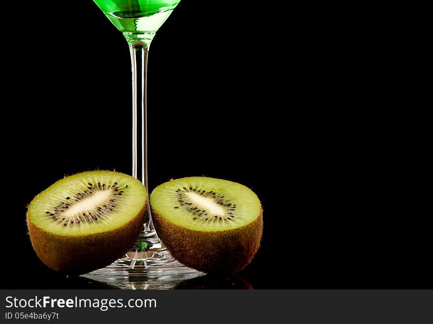 Glass filed with green beverage and a pieces of kiwi. Black background. Studio shot.