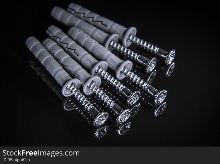 Close up of screws with plastic drywall plugs on black reflecting surface background. Close up of screws with plastic drywall plugs on black reflecting surface background.