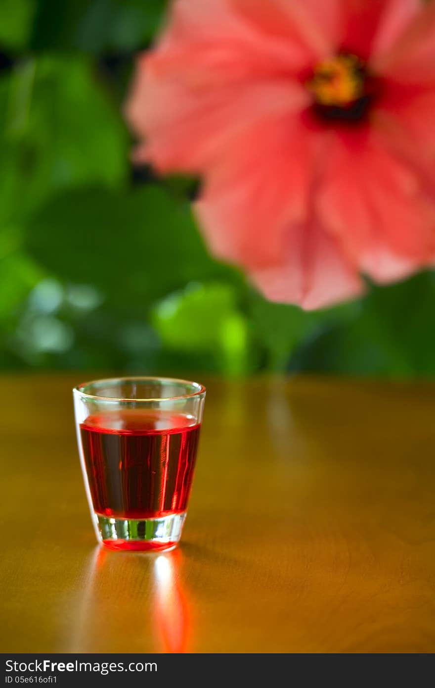 On the table a small glass with liquor, the background - a flower