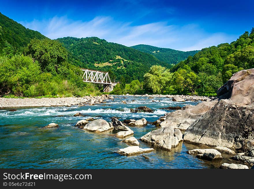 Shore of a mountain river with stones and iron bridge