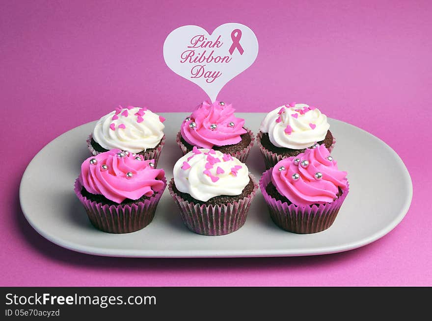 Pink Ribbon Day message across white heart toppers on pink and white decorated red velvet cupcakes on pink background.