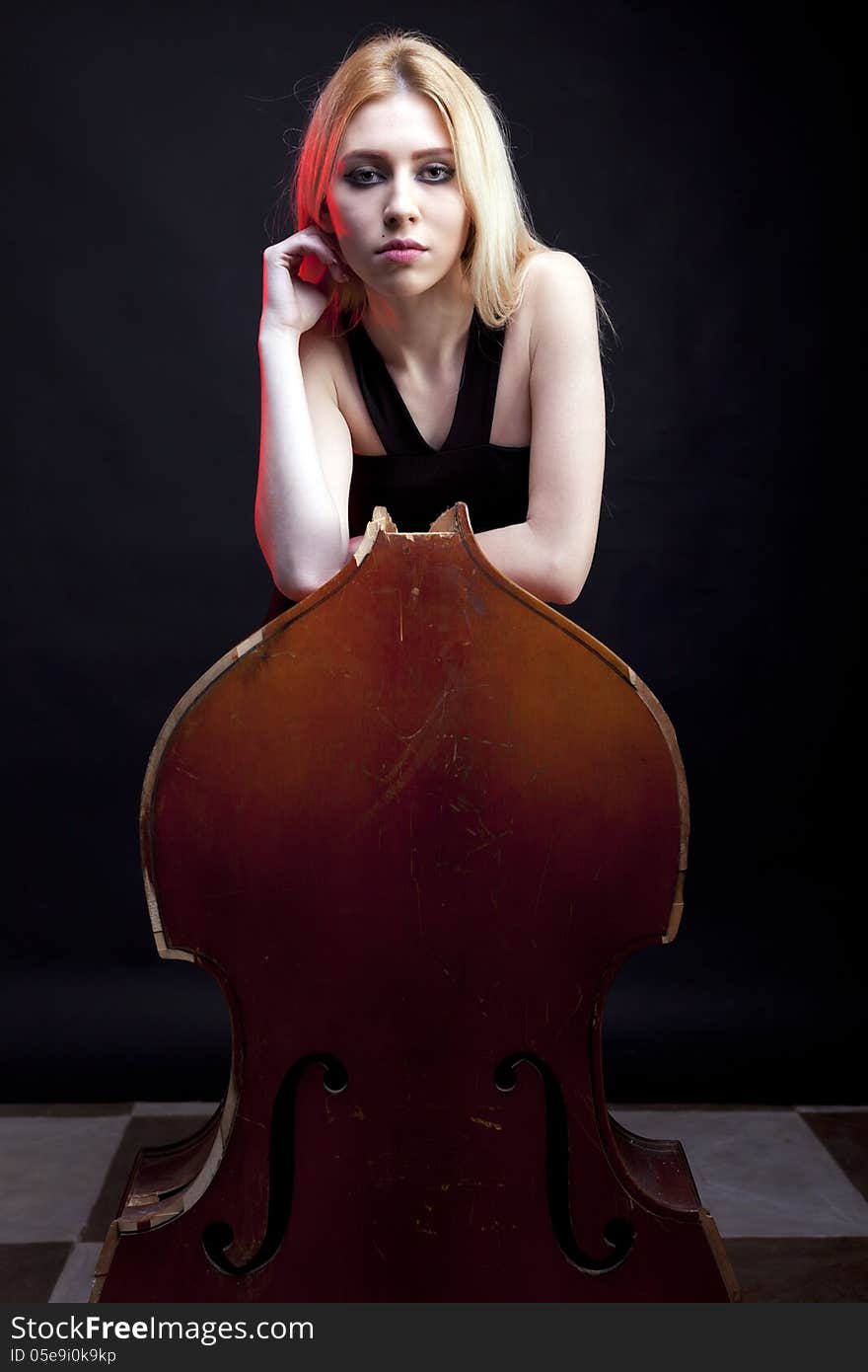 Elegant girl behind a broken contrabass on black background