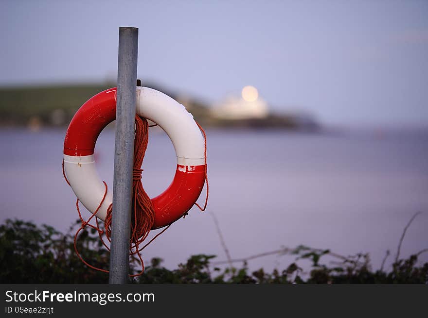 A red and white life ring hanging on a post, overlooking the ocean.