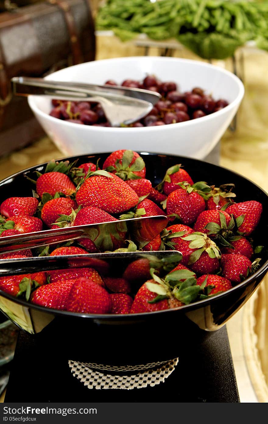 Black bowl of bright red strawberries with green attached. Black bowl of bright red strawberries with green attached.