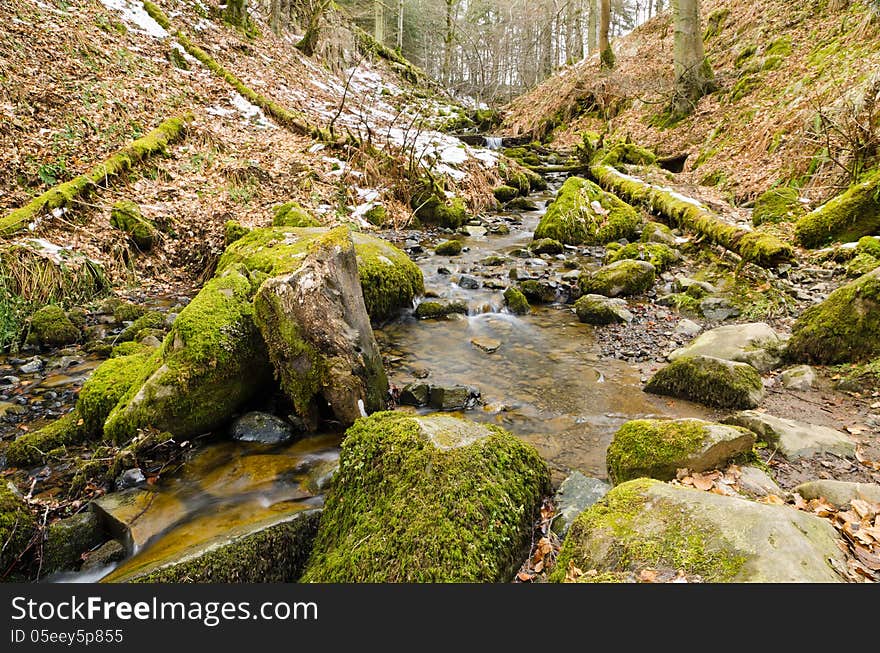 Stream running downhill over moss covered stones in winter. Stream running downhill over moss covered stones in winter