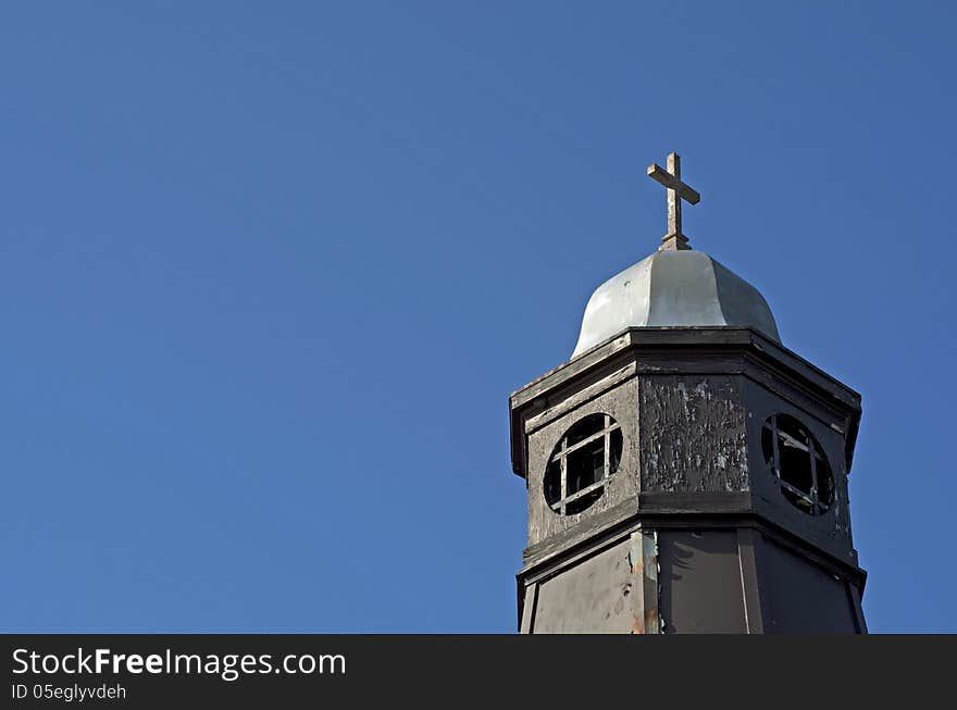 Older church steeple with a steel cross against a clear blue sky. Older church steeple with a steel cross against a clear blue sky