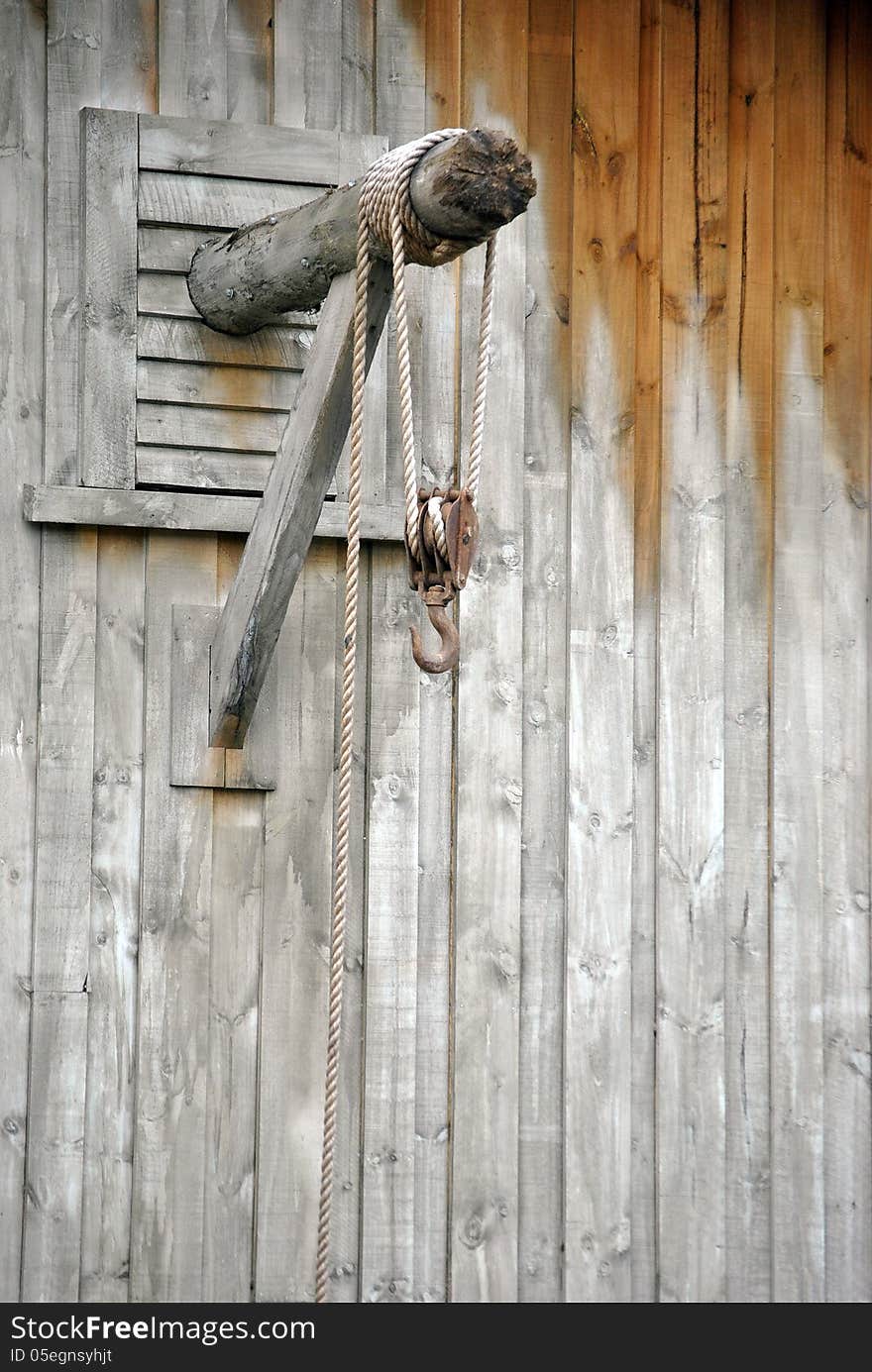 Horizontal pole through wooden wall with long rope rolled around it and iron hook attached to rope. Horizontal pole through wooden wall with long rope rolled around it and iron hook attached to rope