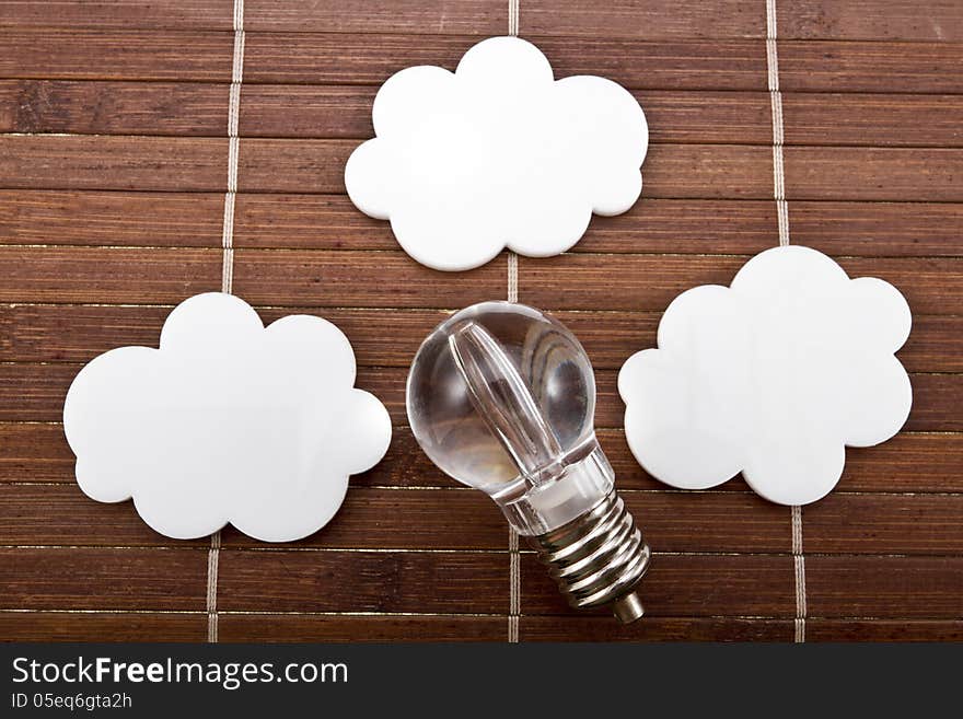 Light bulb with white speech bubbles in a shape of cloud on a wood background.