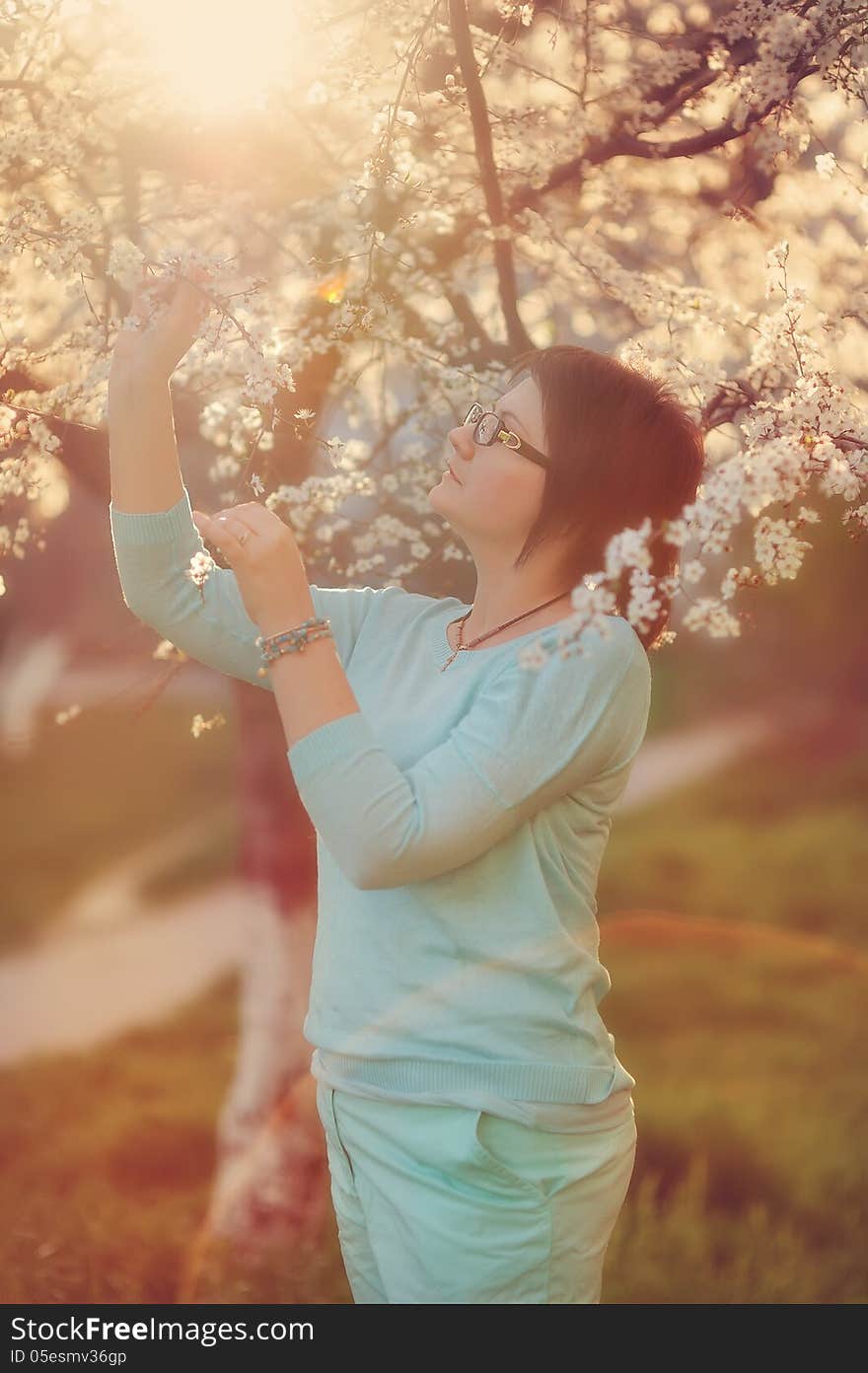 Girl in glasses on a background of a blossoming tree in spring in the garden