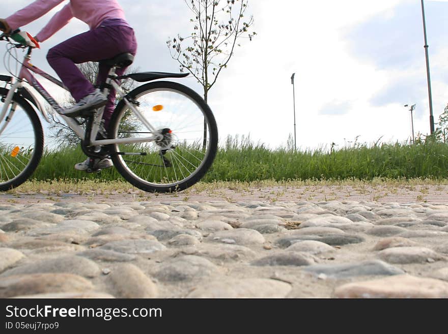 Stony road shot from below with a little girl cyclist pedaling in nature in the background, outdoor. Stony road shot from below with a little girl cyclist pedaling in nature in the background, outdoor