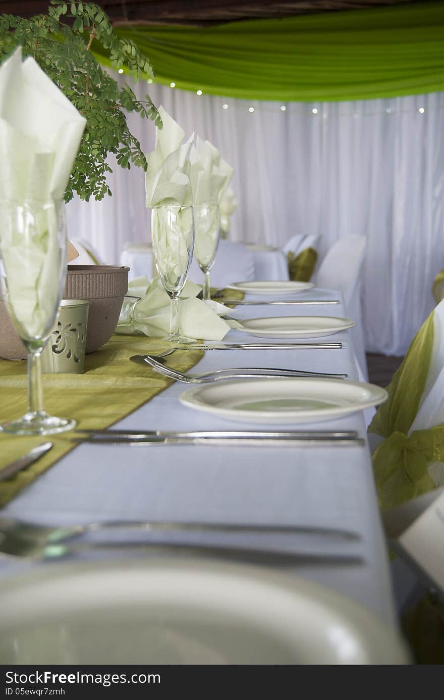 A horizontal image of a wedding table setting with a green theme and depth of field focused on the center of the image.