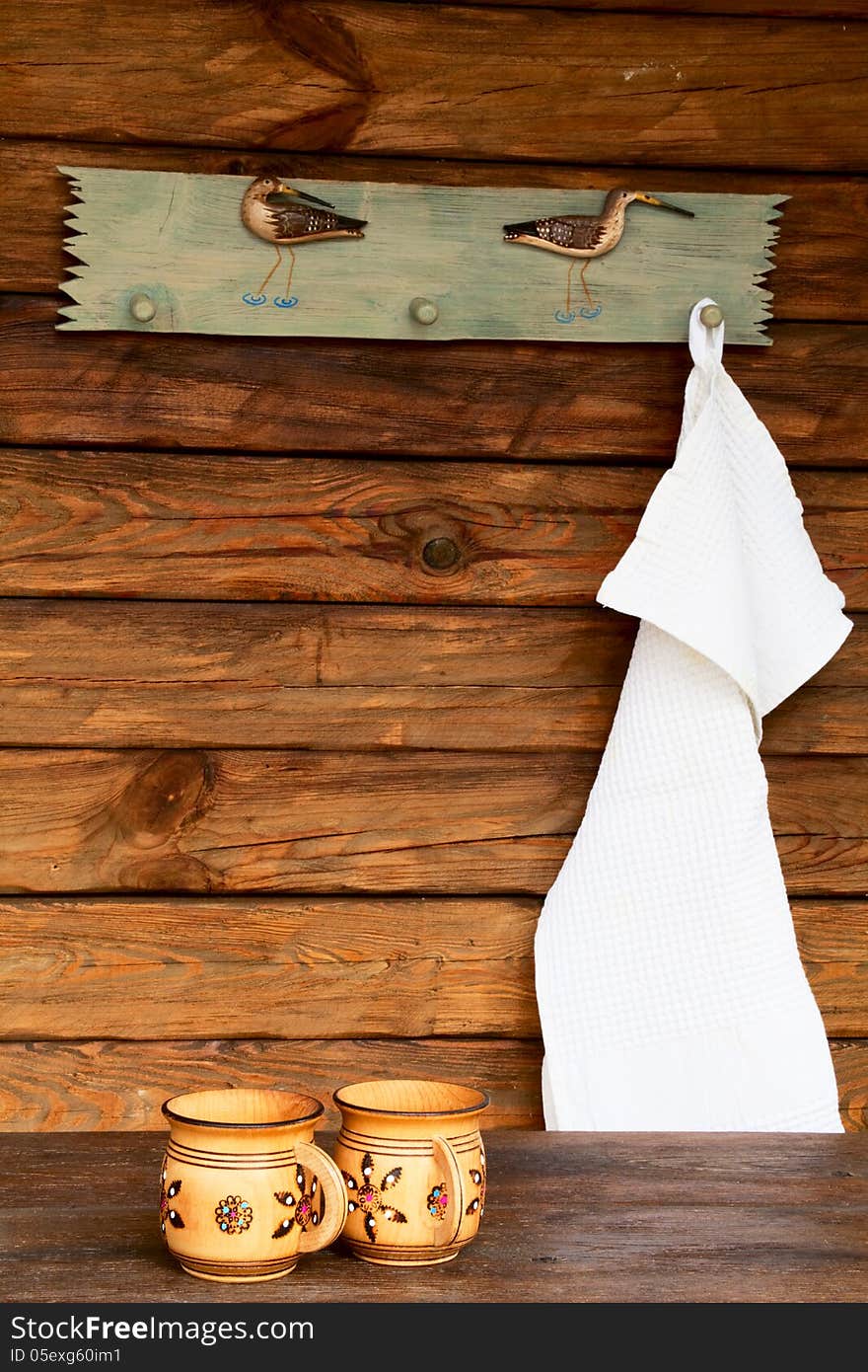 Two wooden mugs with ornaments and a white towel on the background a wooden wall. Two wooden mugs with ornaments and a white towel on the background a wooden wall