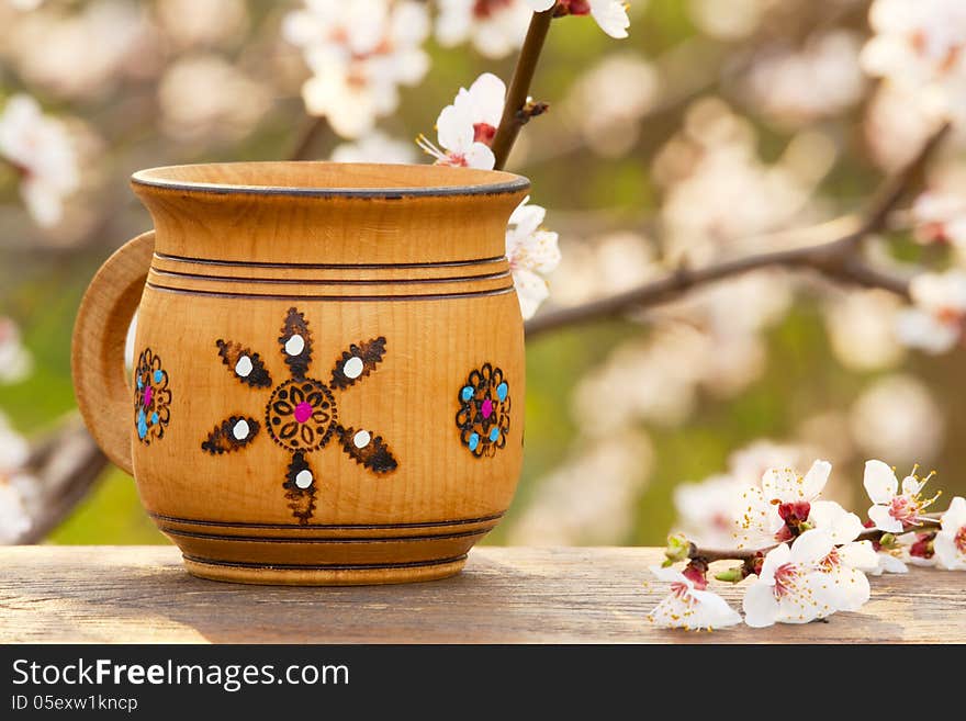 Wooden mug with an ornament in the sunlight on the background a blossoming tree