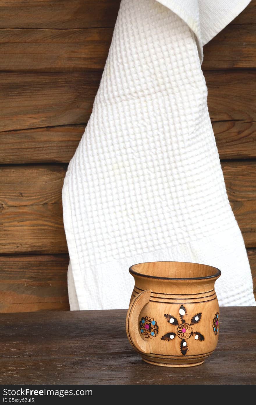 Wooden mug with ornament and a white towel on the background a wooden wall. Wooden mug with ornament and a white towel on the background a wooden wall