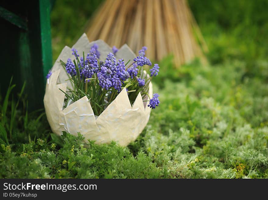 On the green grass in the pot as a white egg with blue flowers. On the green grass in the pot as a white egg with blue flowers