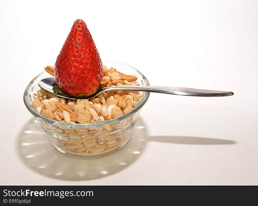 A strawberry on a spoon on a glass bowl of cereal. A strawberry on a spoon on a glass bowl of cereal.