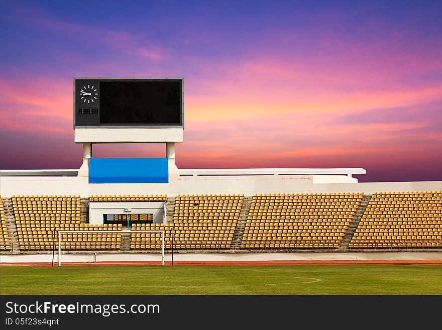 Rows of orange seats on the stadium with scoreboard displaying clock above them