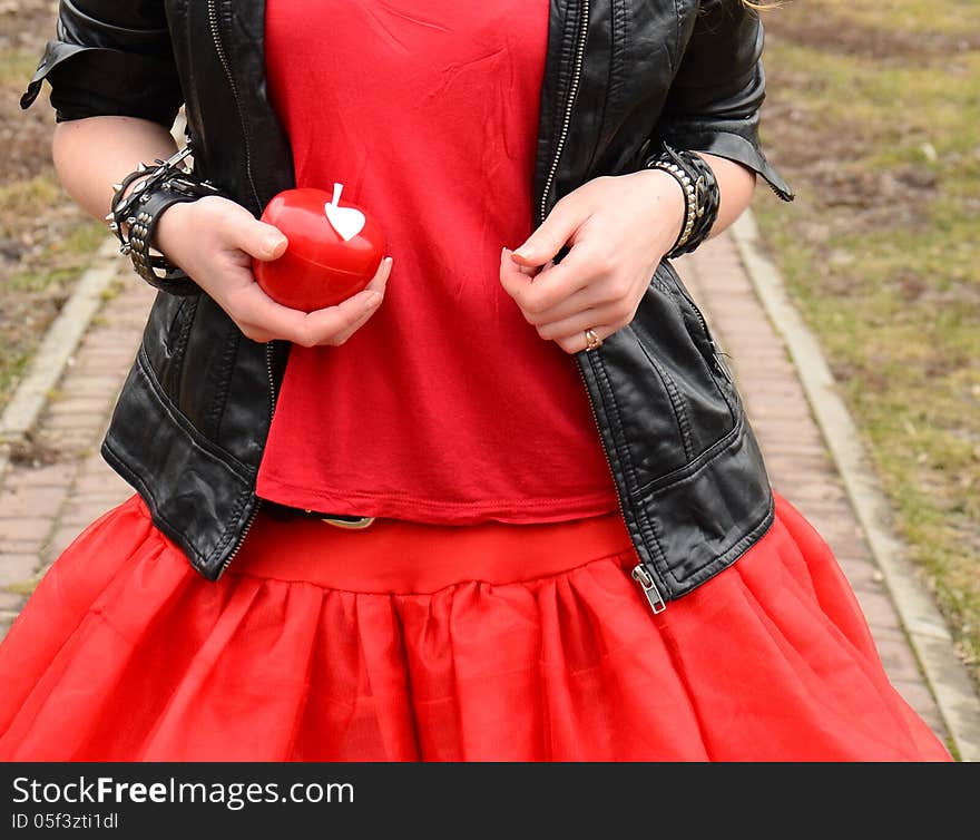 A red apple in a hand of a girl in a red dress with black jacket