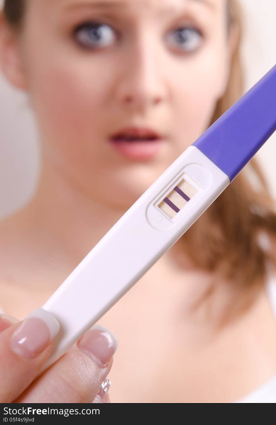 Cute girl is showing her positive pregnancy test. The girl is surprised.