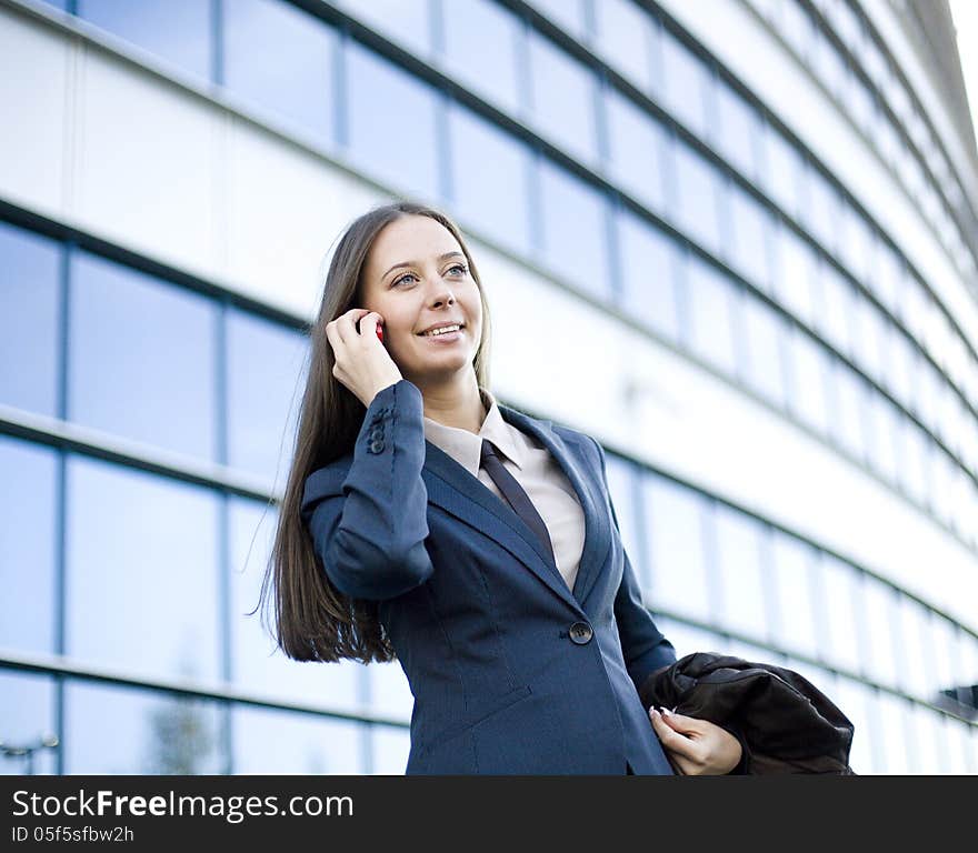 Portrait of pretty young business woman talking on phone near building, talking