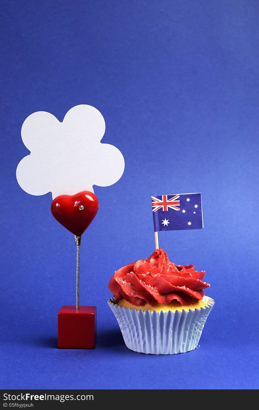 Australian theme red, white and blue cupcake with national flag, and sign for your text here, for Australia Day, Anzac Day or national holiday against a blue background. Vertical with copy space for your text here. Australian theme red, white and blue cupcake with national flag, and sign for your text here, for Australia Day, Anzac Day or national holiday against a blue background. Vertical with copy space for your text here.