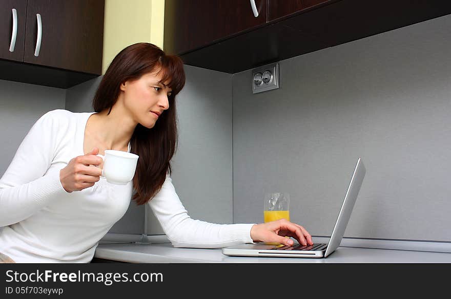 Woman working on a laptop (computer) while drinks coffee and fresh orange juice indoor