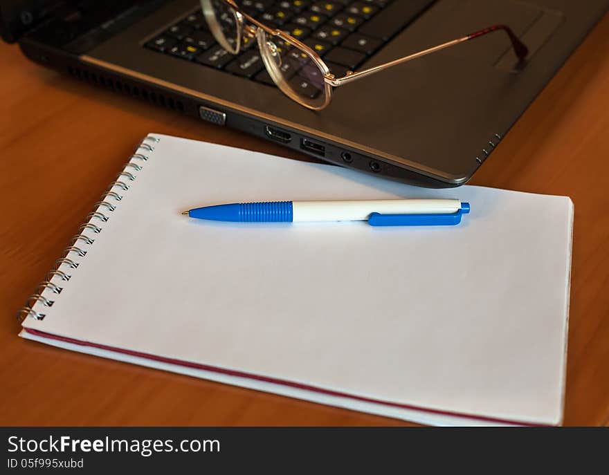 Pen with notebook and glasses near laptop on the table