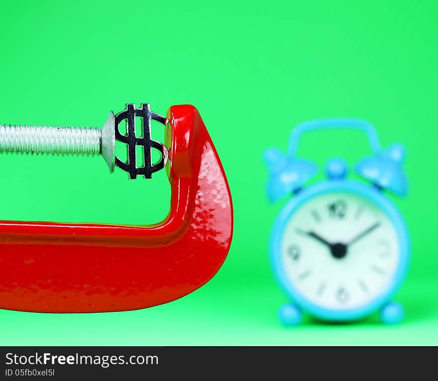 A silver Dollar symbol placed in a red clamp with a pastel green background, with a light blue alarm clock in the background indicating the pressure on dollar. A silver Dollar symbol placed in a red clamp with a pastel green background, with a light blue alarm clock in the background indicating the pressure on dollar.