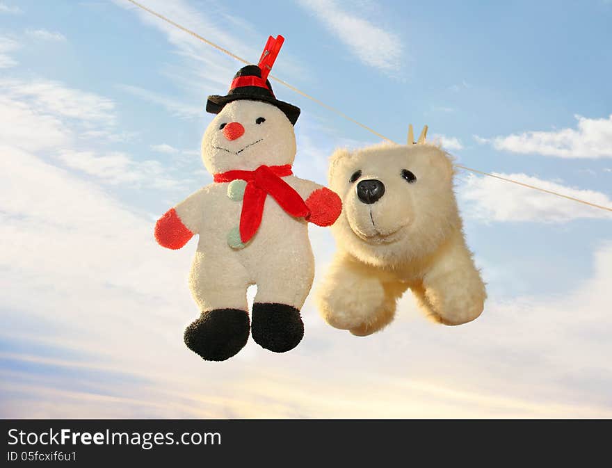 Toy polar bear and snowman hanging on a rope and drying off after washing on the background of a gentle spring sky. Toy polar bear and snowman hanging on a rope and drying off after washing on the background of a gentle spring sky