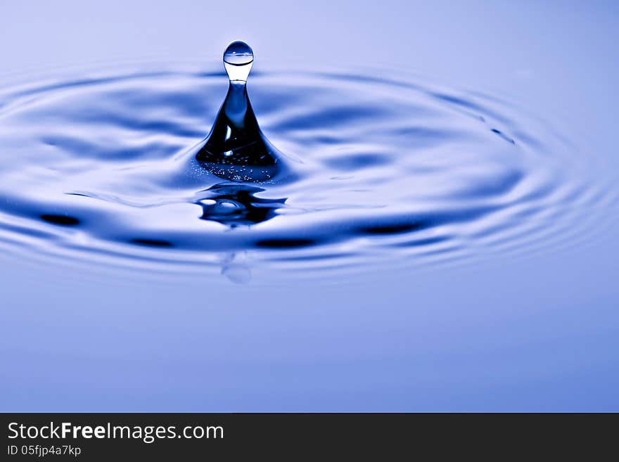 Conical water droplet suspended in the air breaking the surface of the liquid with a radiating wave