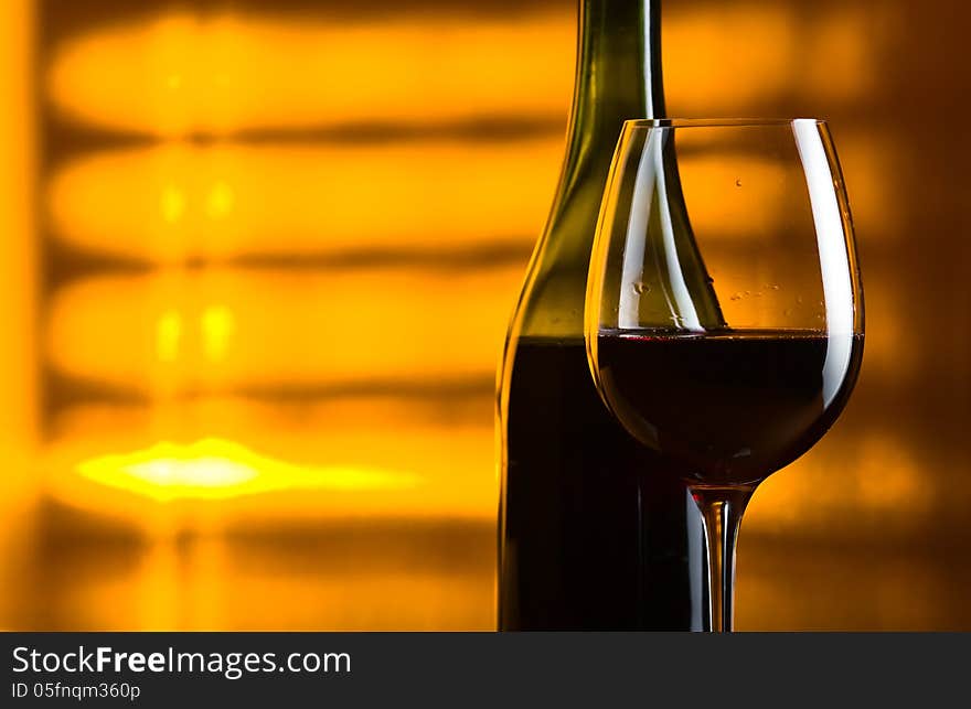 Bottle and glass with red wine on a yellow background