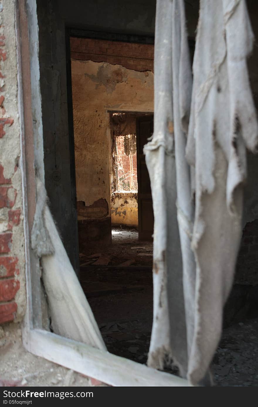 View of the inside of an abandoned building, a shabby curtain is in the front, in the background rooms with scrapped walls