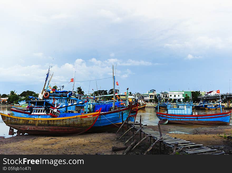 Fishing boats in harbor with the jetty at foreground and cloudy sky at background