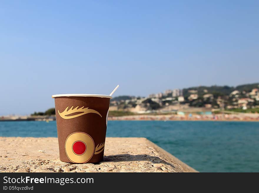 Paper cup of coffee on the beach with sea as a background.