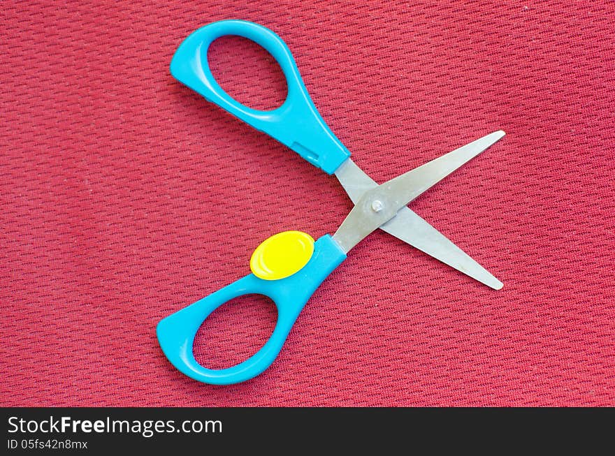 Opened colorful scissor on red textile background