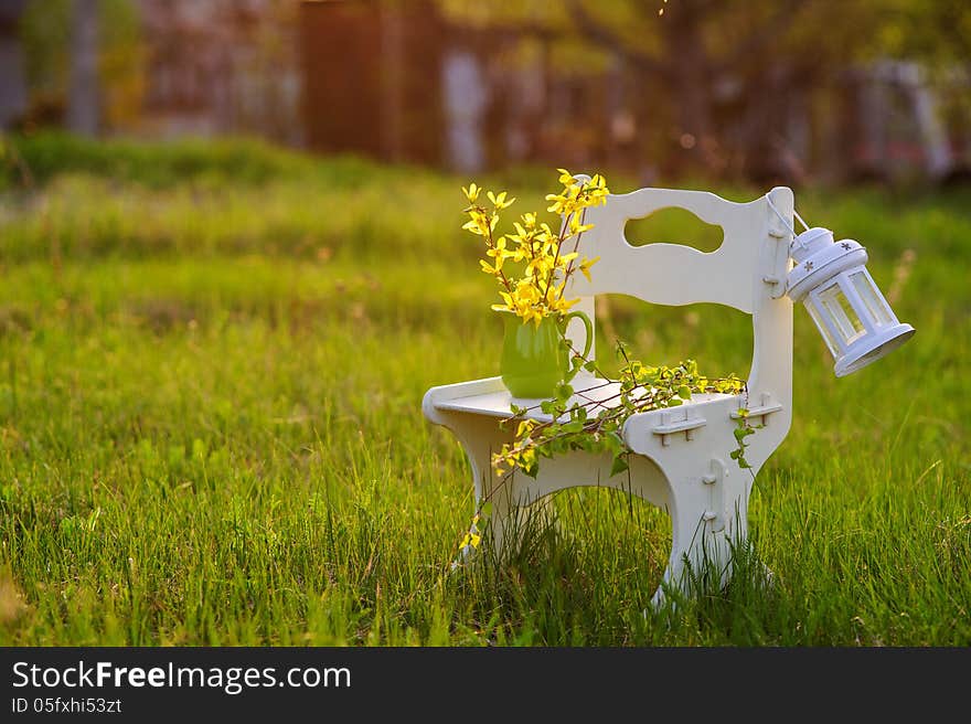 White wooden chair with flowers and white decorative lantern in the sunset light. White wooden chair with flowers and white decorative lantern in the sunset light