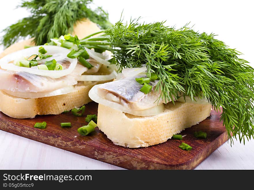 Sandwiches of white bread with herring, onions and herbs on wooden board