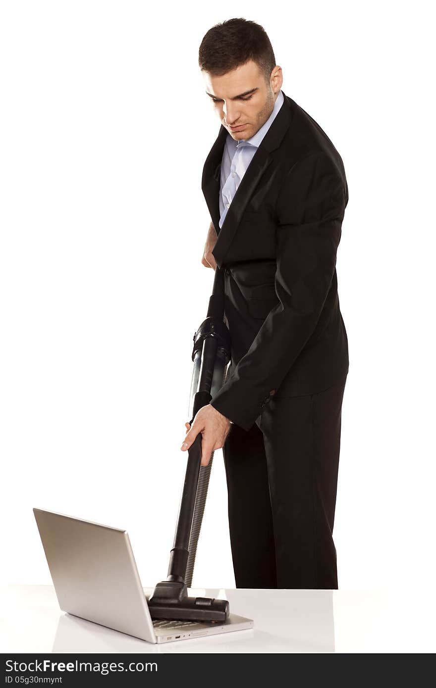 Serious and attractive young businessman vacuum cleans his laptop. Serious and attractive young businessman vacuum cleans his laptop