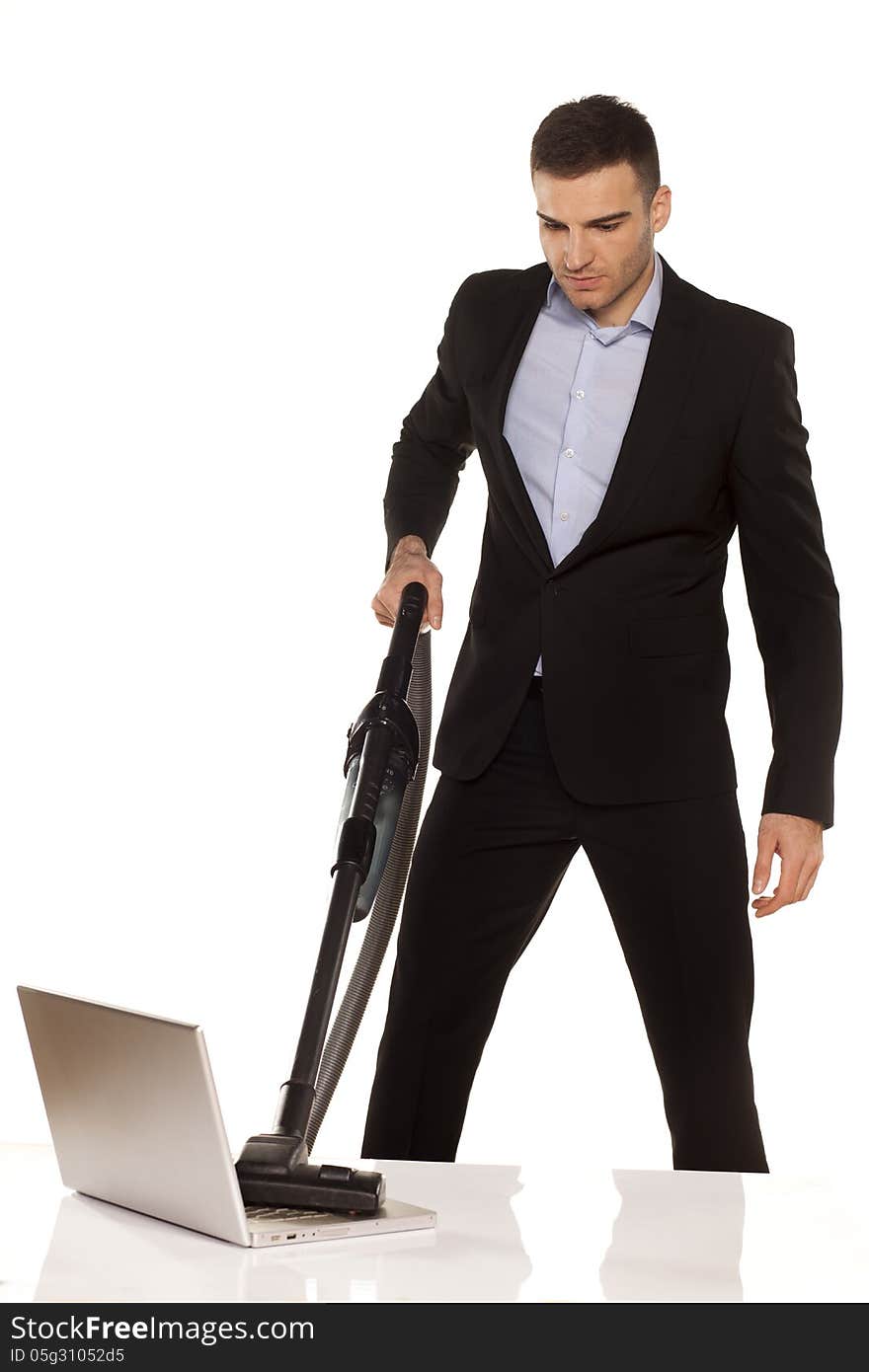 Serious and attractive young businessman vacuum cleans his laptop. Serious and attractive young businessman vacuum cleans his laptop