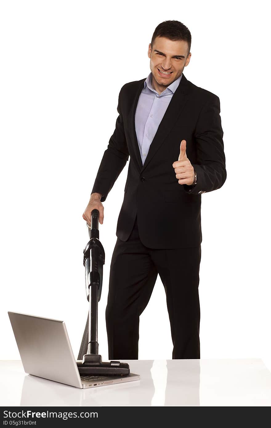 Smiling and attractive young businessman vacuum cleans his laptop and showing thumbs up. Smiling and attractive young businessman vacuum cleans his laptop and showing thumbs up