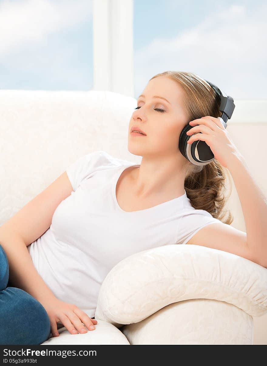 Woman in headphones enjoys music while lying on the sofa at home