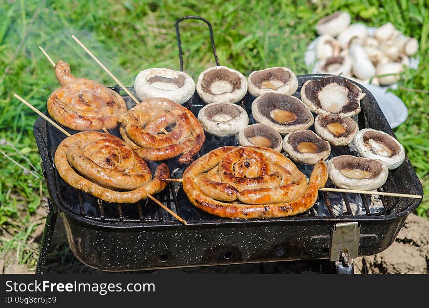 Champignon mushrooms and sausages cooking on barbecue in garden. Champignon mushrooms and sausages cooking on barbecue in garden.