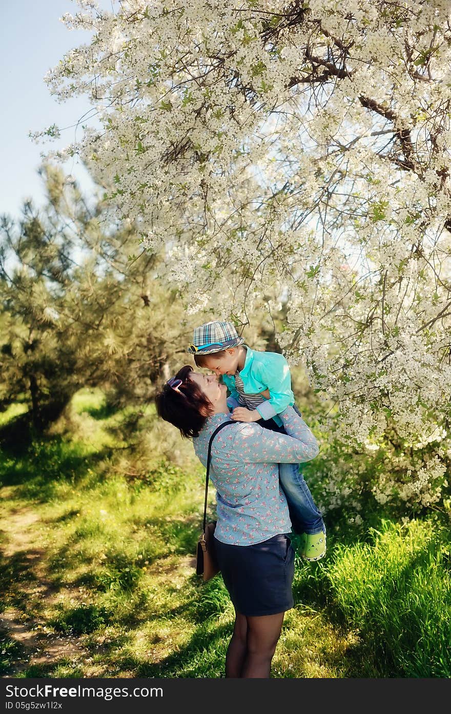 In nature in a lush garden a little boy in the blue shirt in the hands of mother. In nature in a lush garden a little boy in the blue shirt in the hands of mother