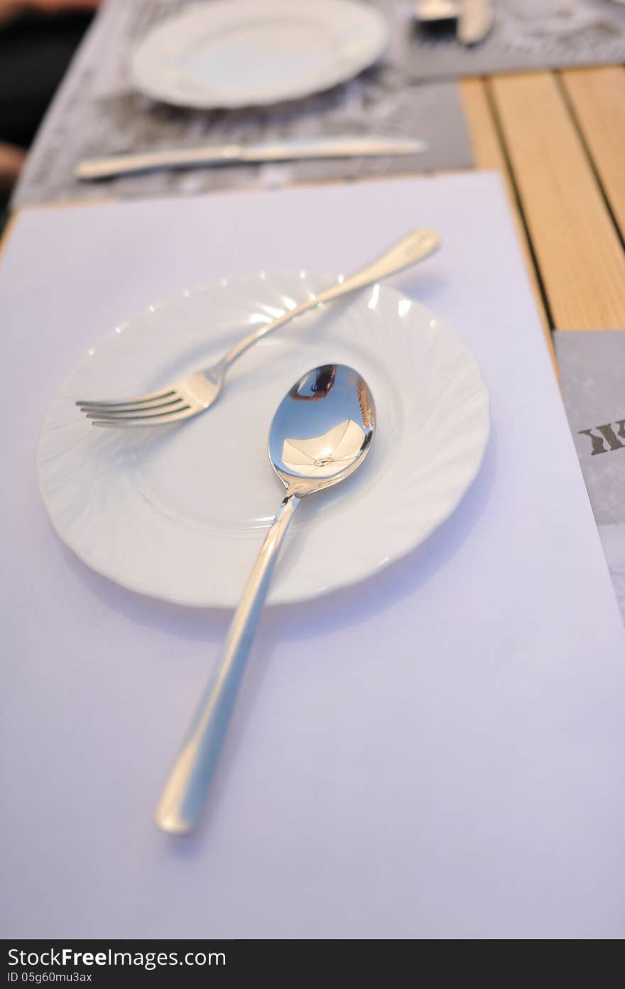 On a white napkin is white plate with a spoon and fork. On a white napkin is white plate with a spoon and fork