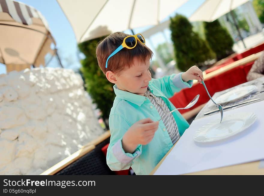 Stylish little boy with sunglasses sitting at a table in a restaurant. Stylish little boy with sunglasses sitting at a table in a restaurant