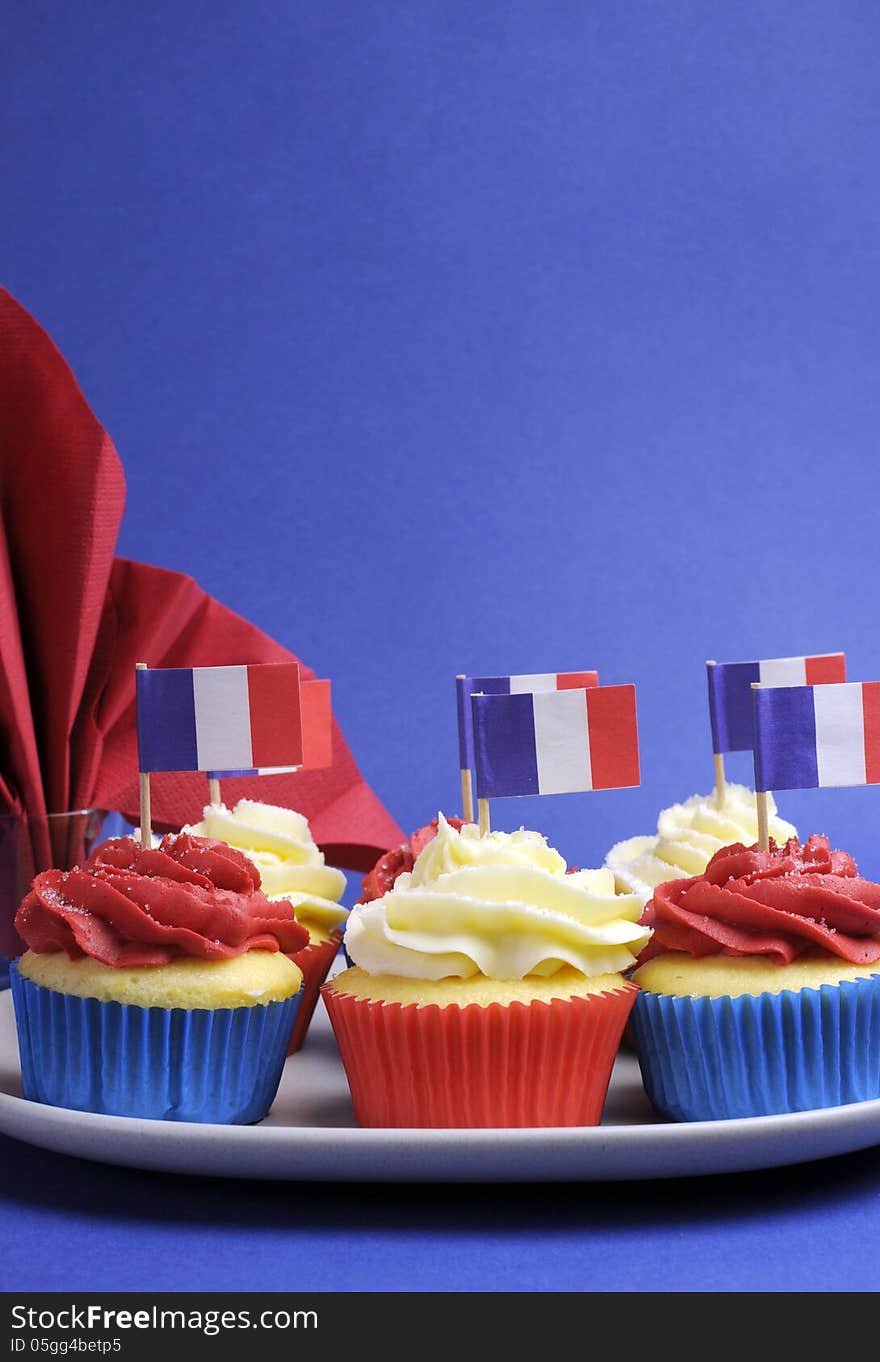 French theme red, white and blue mini cupcake cakes with flags of France and fleur-de-lis red napkin for National holidays of France, Bastille Day, the Fourteenth of July. Vertical with copy space for your text here. French theme red, white and blue mini cupcake cakes with flags of France and fleur-de-lis red napkin for National holidays of France, Bastille Day, the Fourteenth of July. Vertical with copy space for your text here.