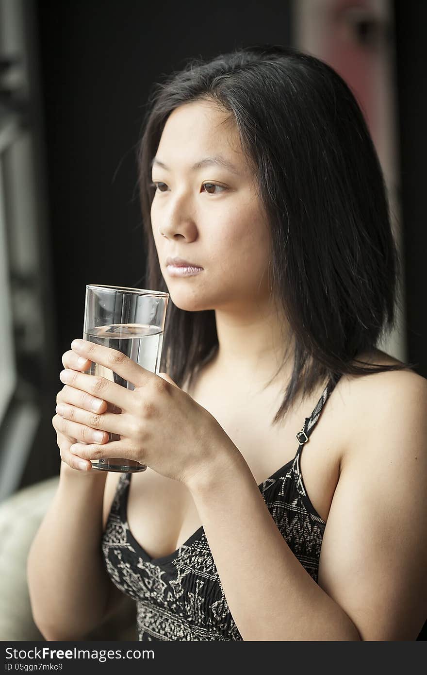 Beautiful Asian woman with brown hair and eyes drinking water from a glass. Beautiful Asian woman with brown hair and eyes drinking water from a glass.