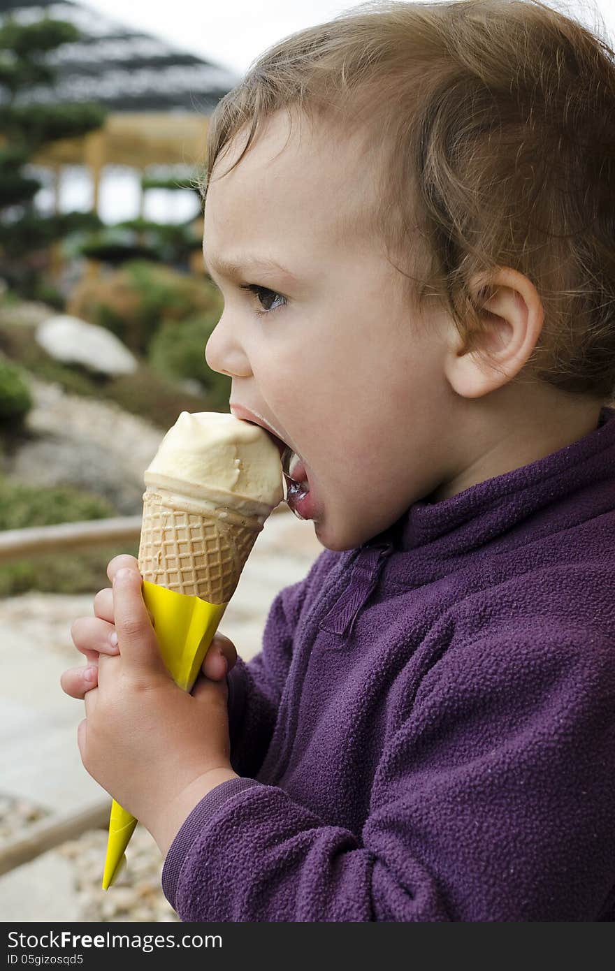 Child toddler, boy or girl, eating ice cream in a cone in a garden. Child toddler, boy or girl, eating ice cream in a cone in a garden.