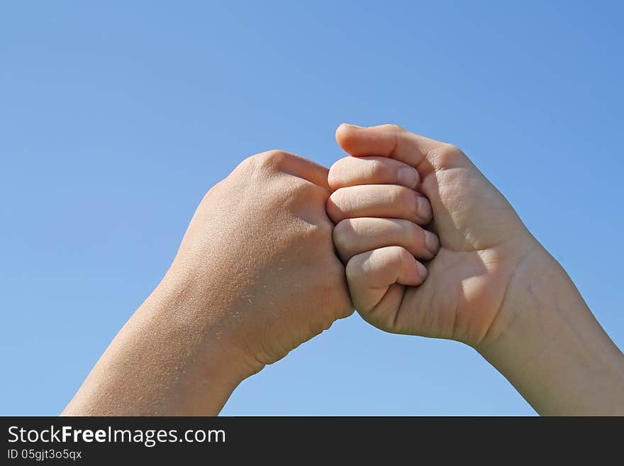 A children's hands on a blue sky background. A children's hands on a blue sky background.