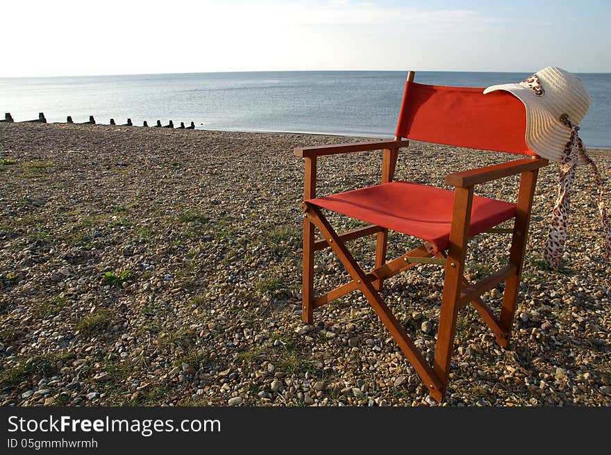 Folding wooden chair on the beach with a straw hat